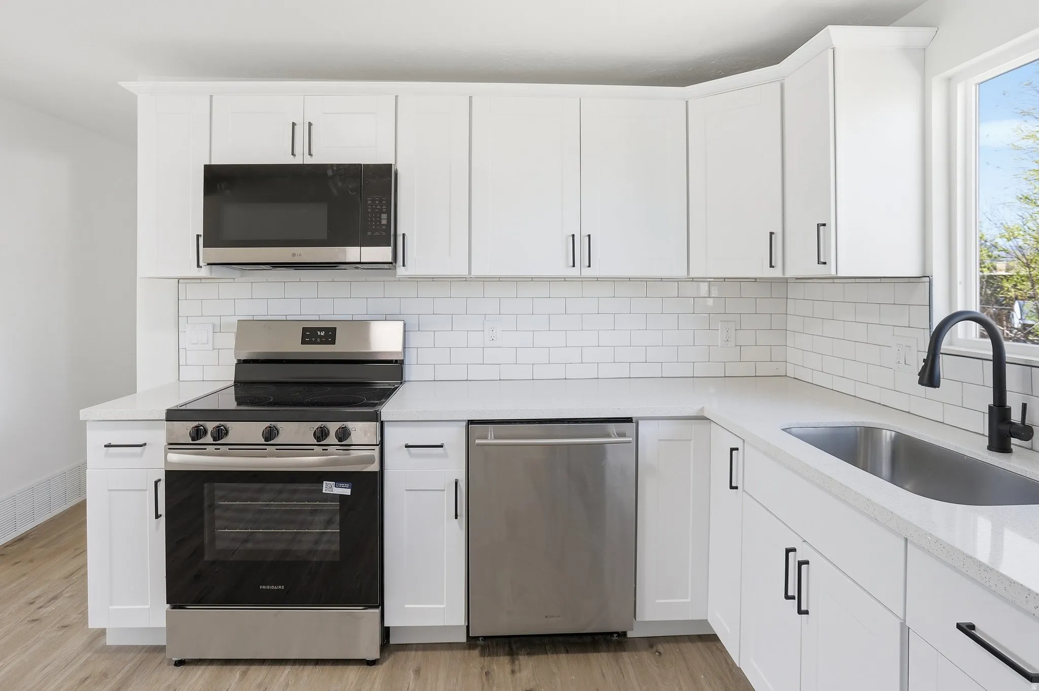 Kitchen featuring stainless steel appliances, white cabinets, backsplash, and light stone countertops