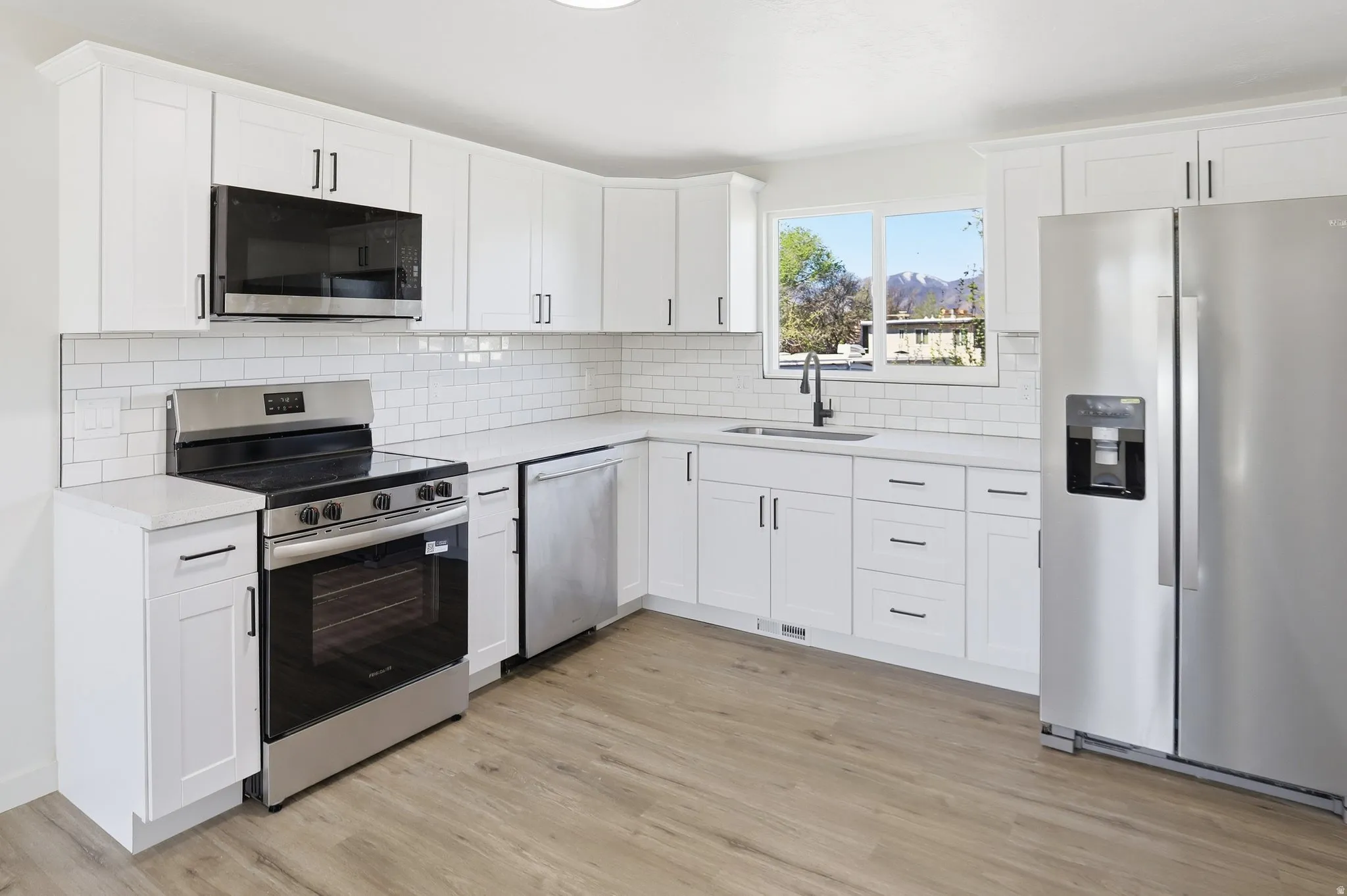 Kitchen with stainless steel appliances, white cabinetry, light wood finished floors, and decorative backsplash