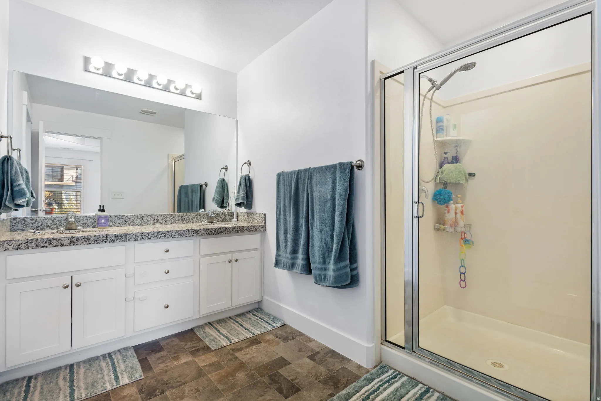 Bathroom with stone finish floors, double vanity, and a stall shower