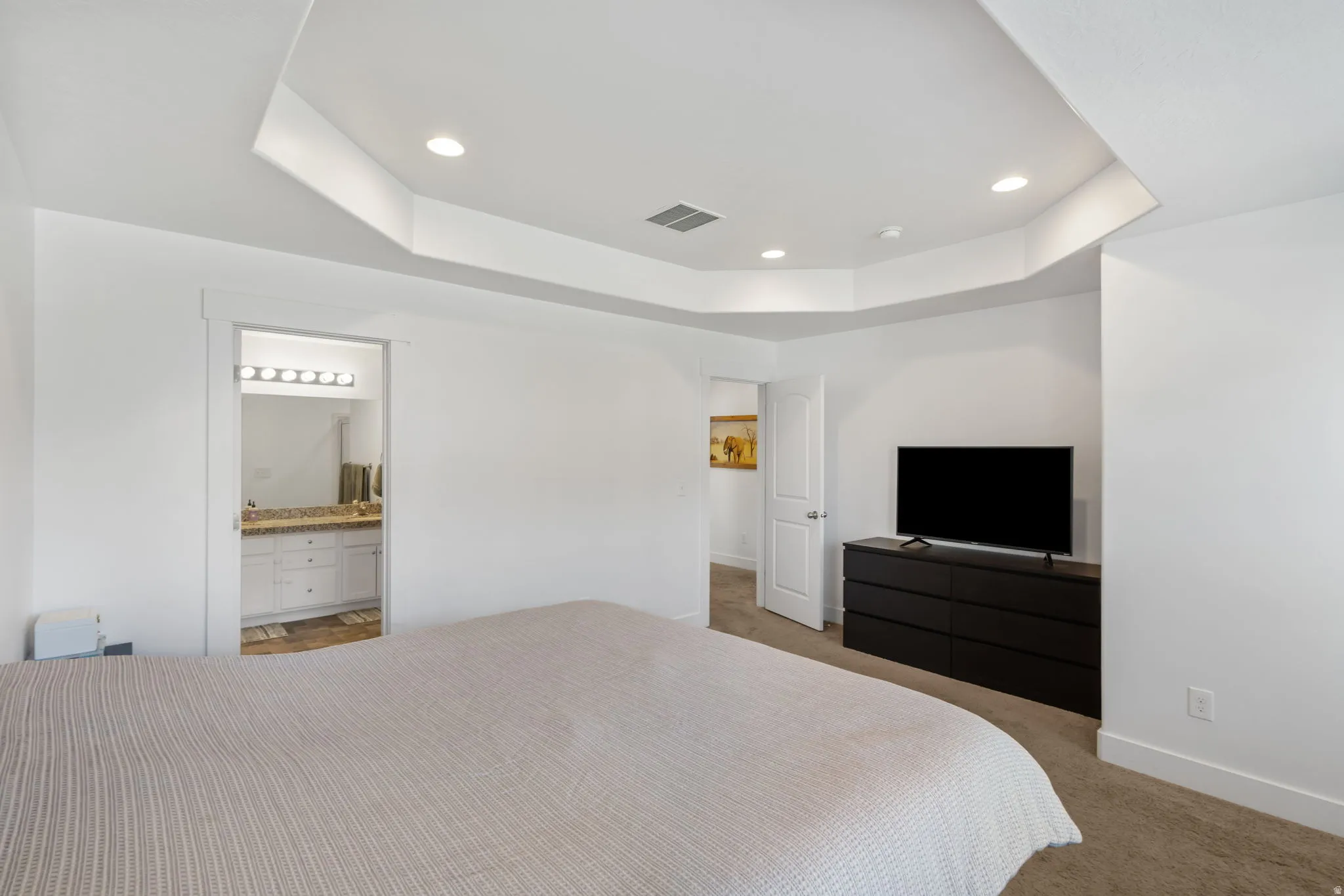 Bedroom featuring a raised ceiling, carpet floors, recessed lighting, and ensuite bathroom