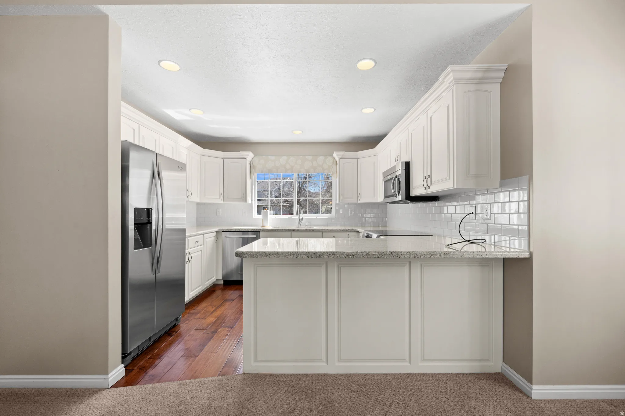 Kitchen featuring a peninsula, stainless steel appliances, white cabinetry, backsplash, and light stone counters