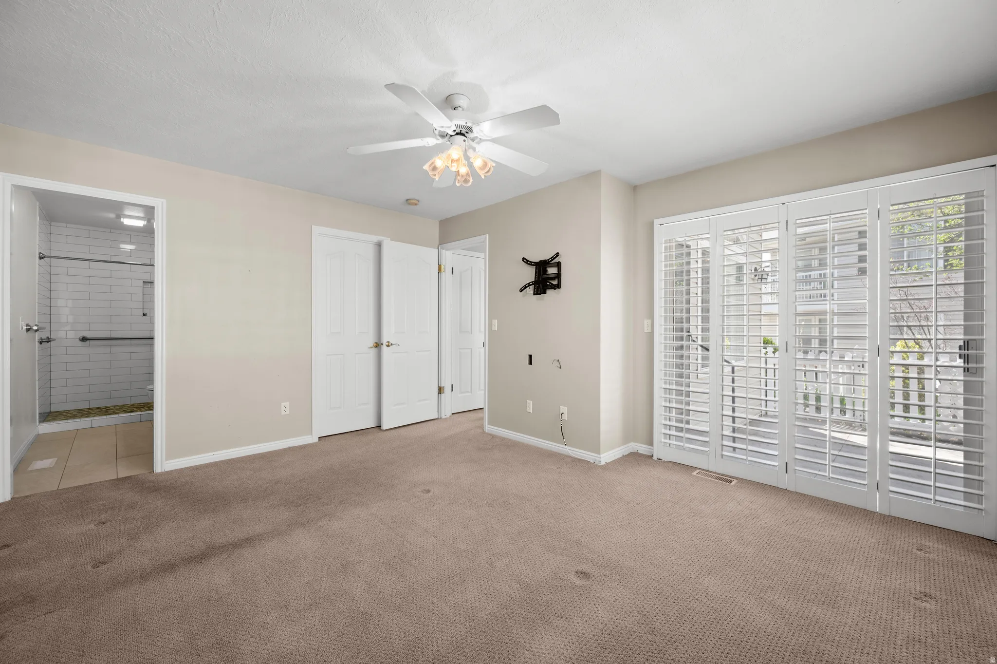 Unfurnished bedroom with access to exterior, light carpet, ensuite bath, and ceiling fan