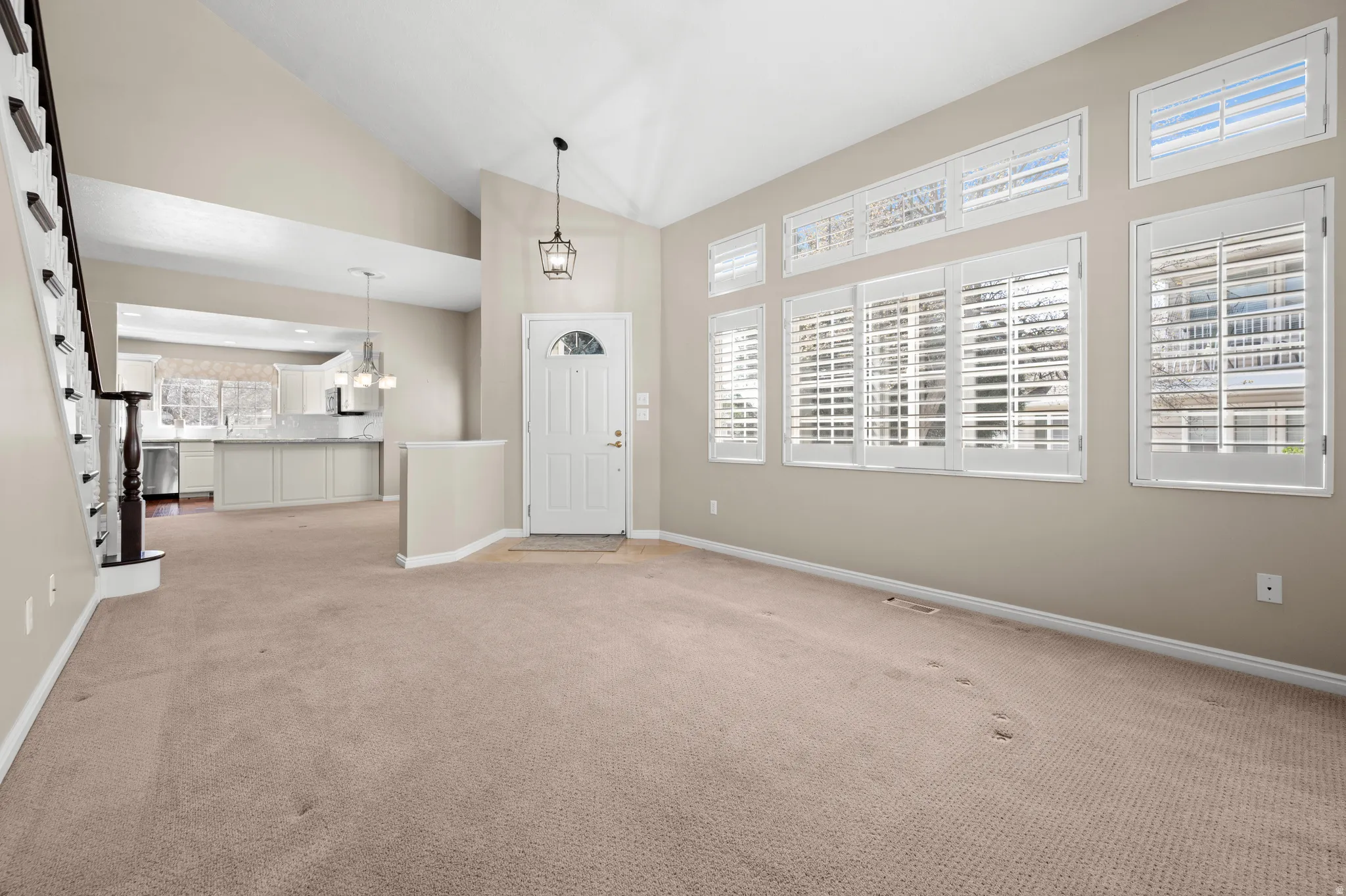 Foyer entrance featuring vaulted ceiling, light colored carpet, and hanging lights