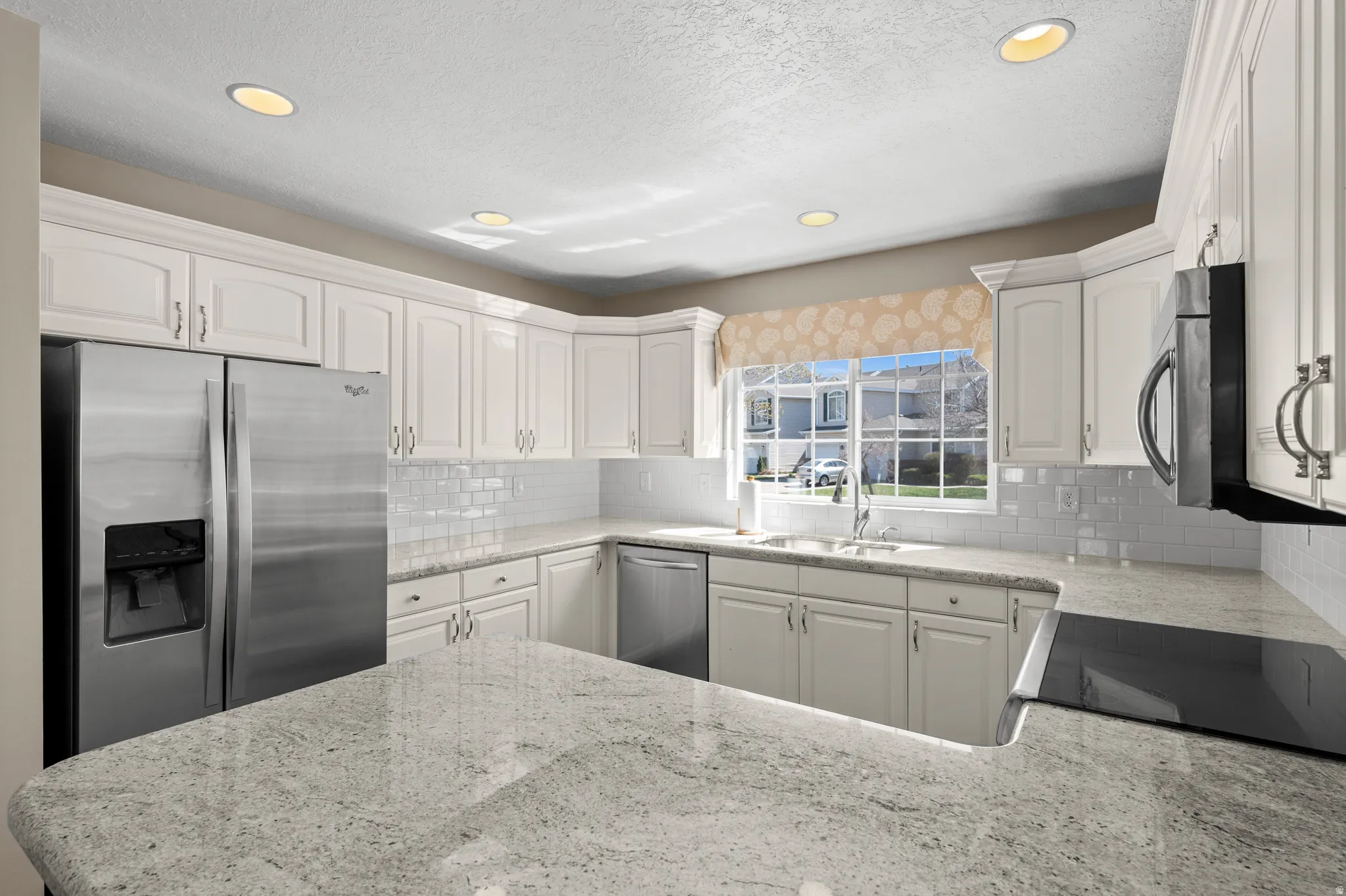 Kitchen featuring stainless steel appliances, white cabinetry, light stone countertops, backsplash, and recessed lighting