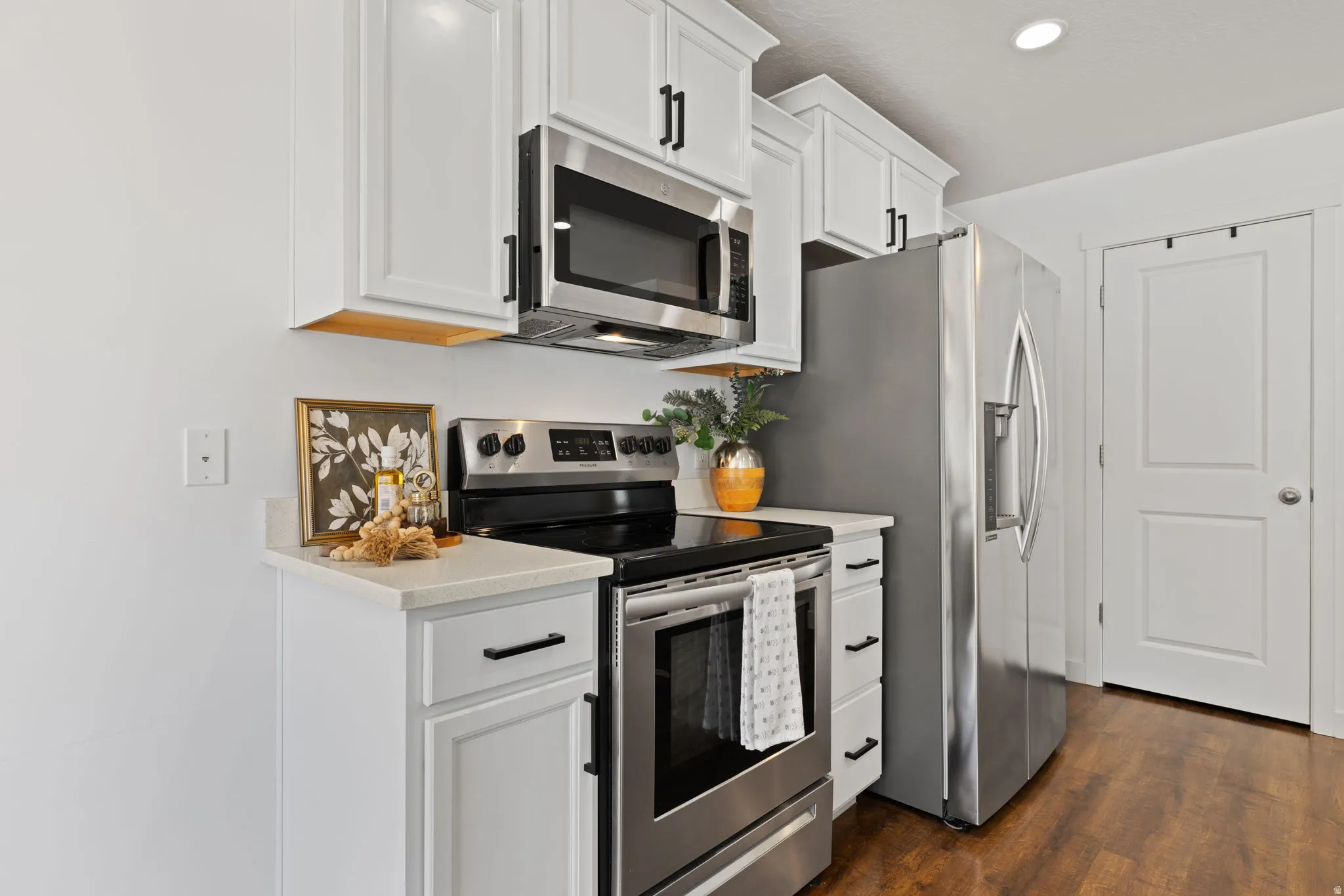 Kitchen featuring stainless steel appliances, white cabinets, dark wood finished floors, recessed lighting, and light stone counters
