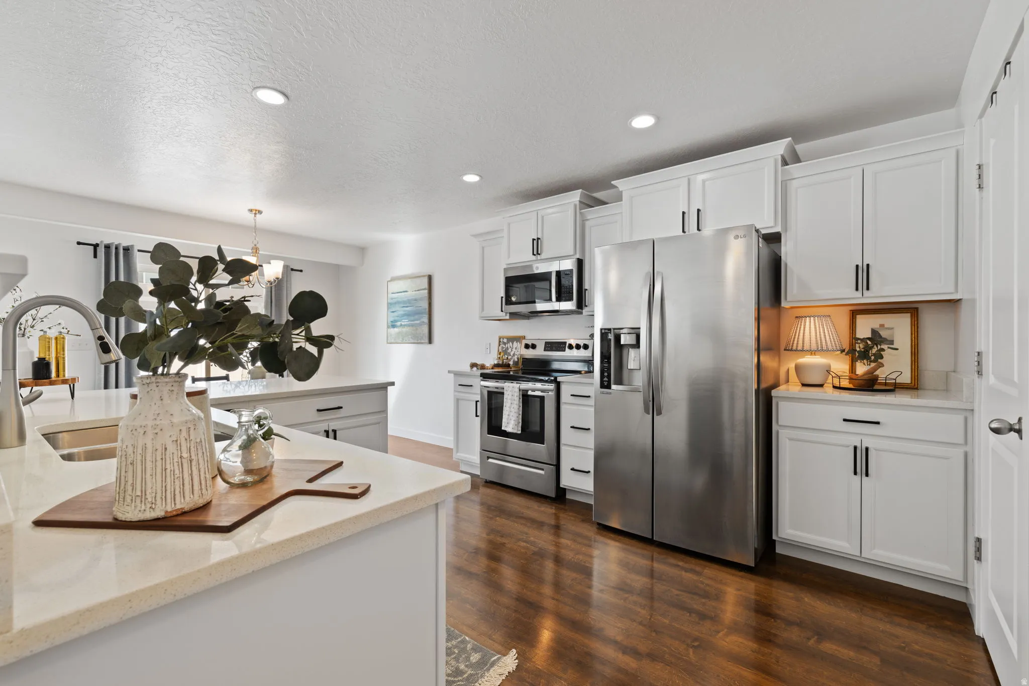 Kitchen with stainless steel appliances, white cabinets, light stone countertops, dark wood finished floors, and a textured ceiling
