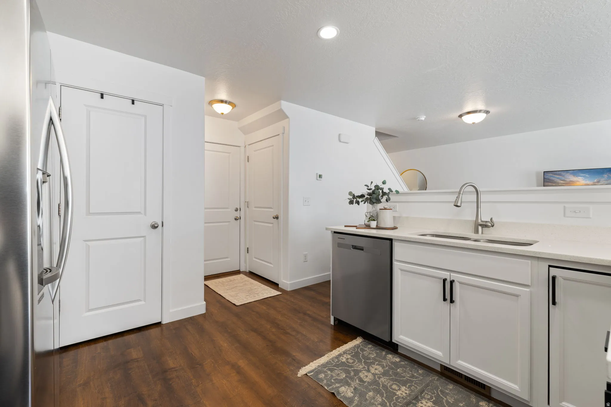Kitchen with stainless steel appliances, white cabinets, light stone counters, dark wood-style flooring, and a textured ceiling