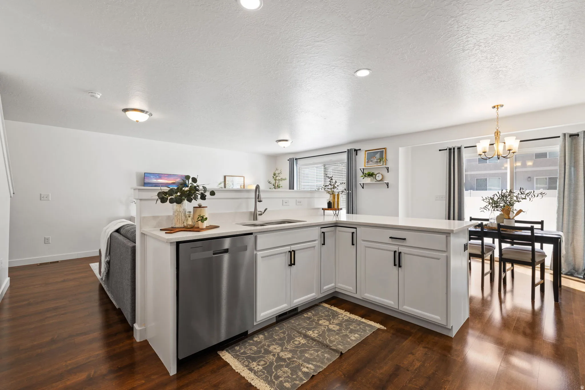 Kitchen featuring a kitchen island with sink, stainless steel dishwasher, white cabinets, dark wood-style flooring, and a textured ceiling