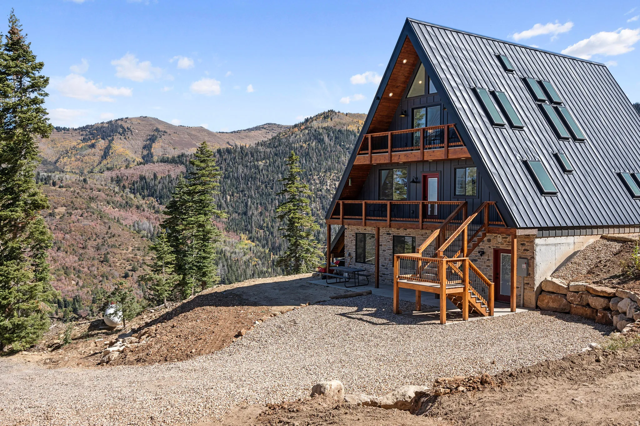 Rear view of house featuring a mountain view, stone siding, board and batten siding, a patio area, and a balcony