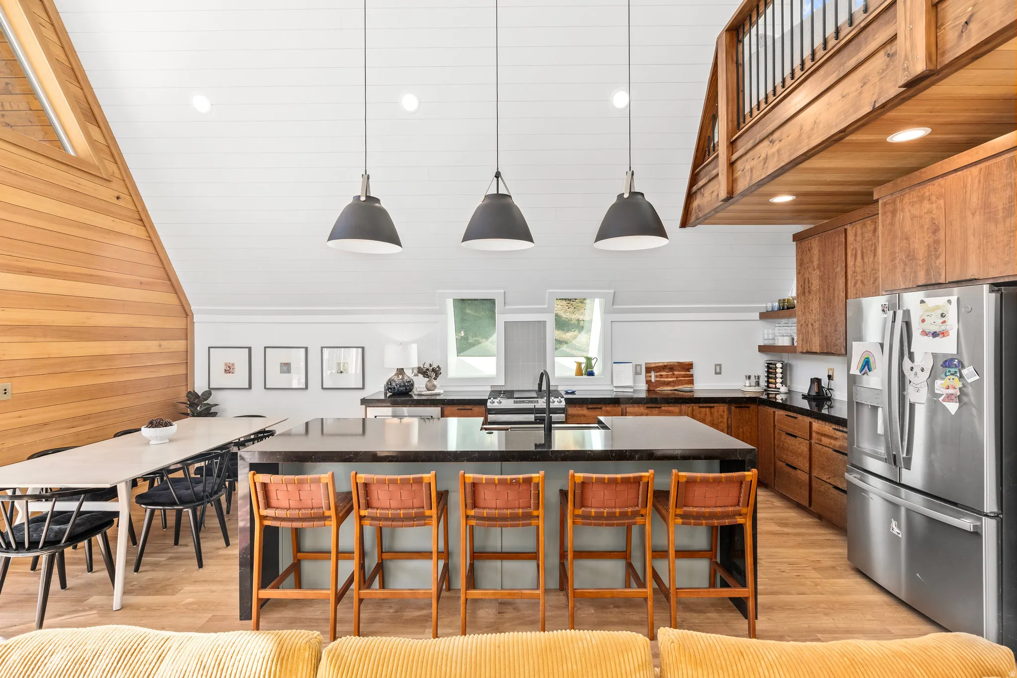 Kitchen with a center island with sink, stainless steel fridge with ice dispenser, pendant lighting, light wood-style flooring, and wooden walls