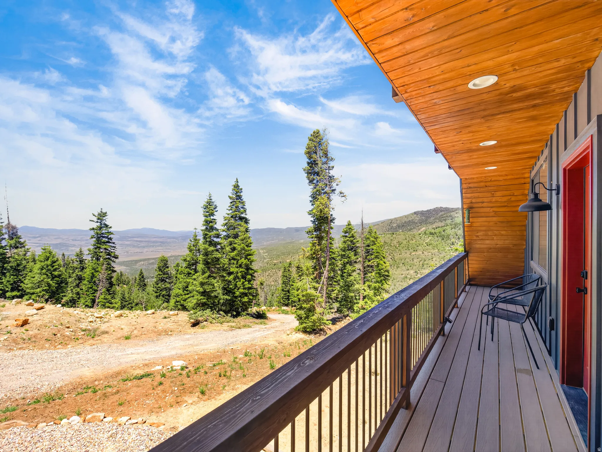 Expansive balcony featuring composite decking, wood-finish railing with glass panels, and a red entry door