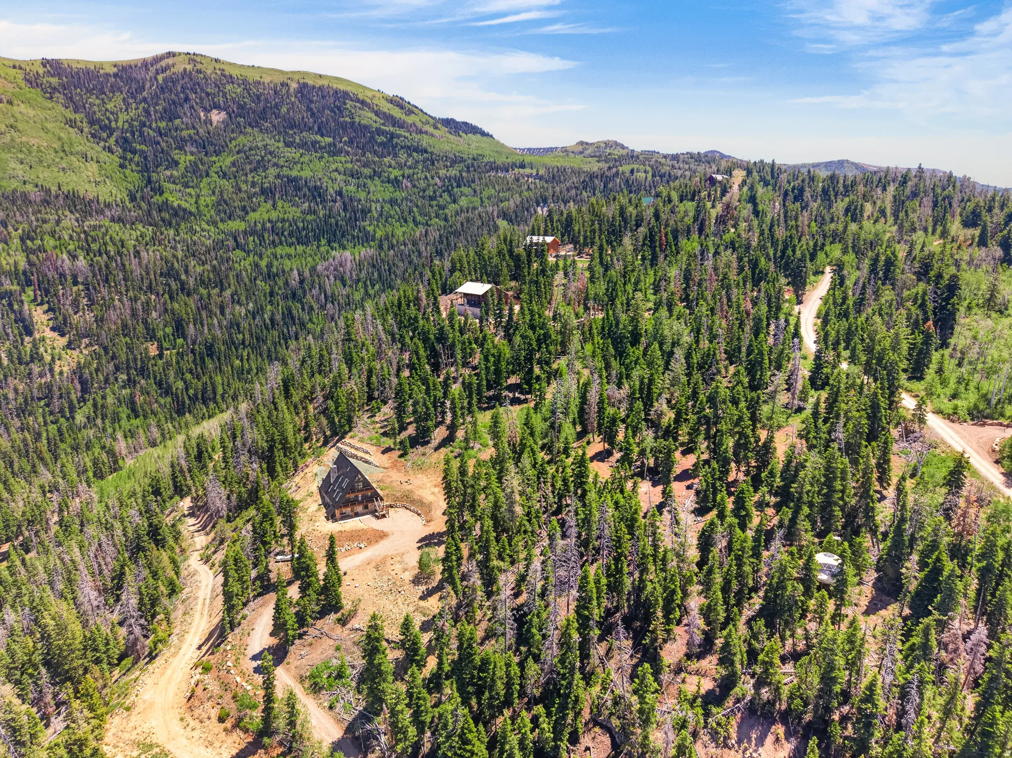 Sprawling wooded property featuring multiple structures, mountain terrain, and winding dirt roads