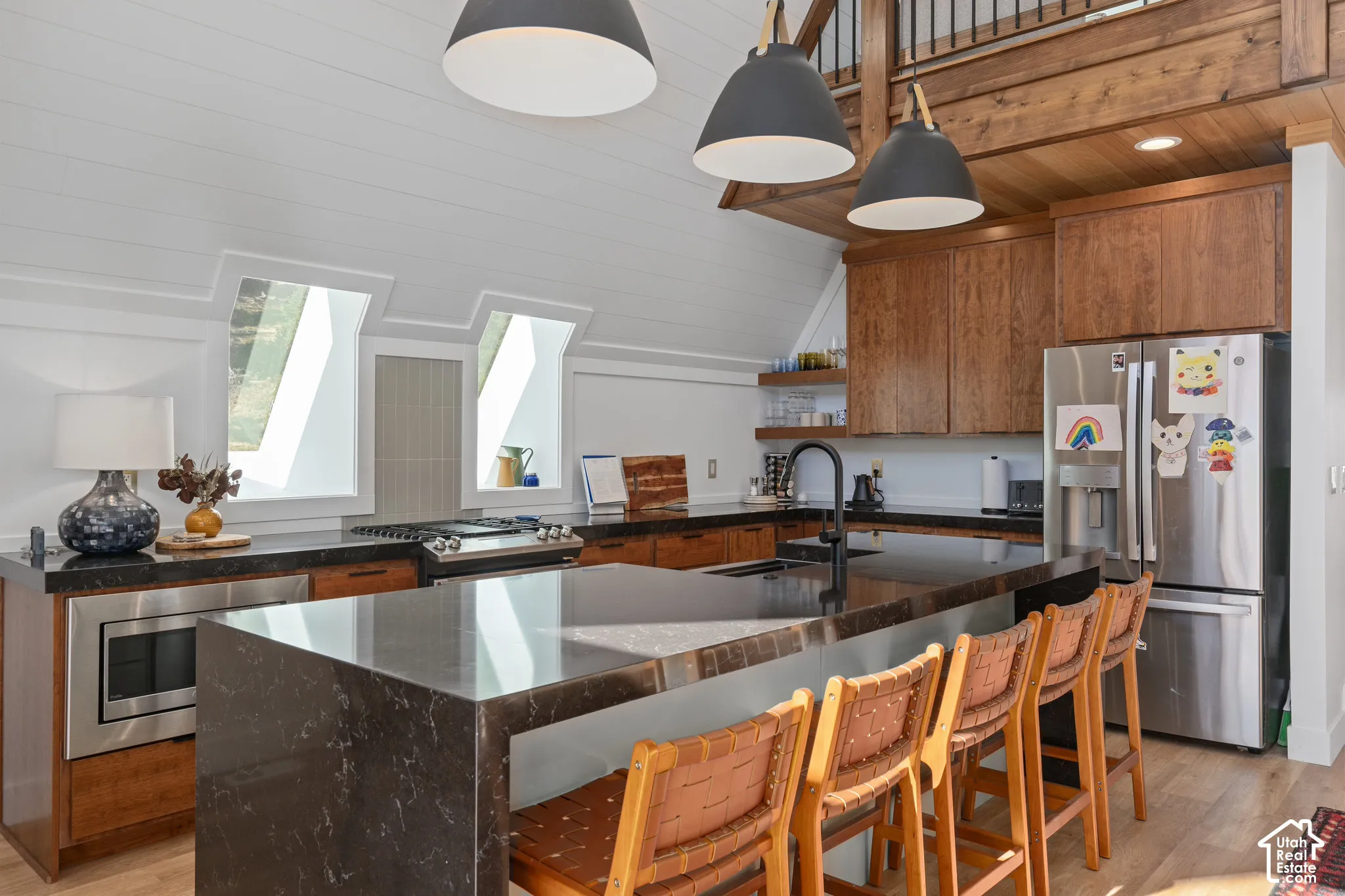 Kitchen featuring light wood-style floors, stainless steel appliances, wood finish cabinets, dark stone counters, and lofted ceiling