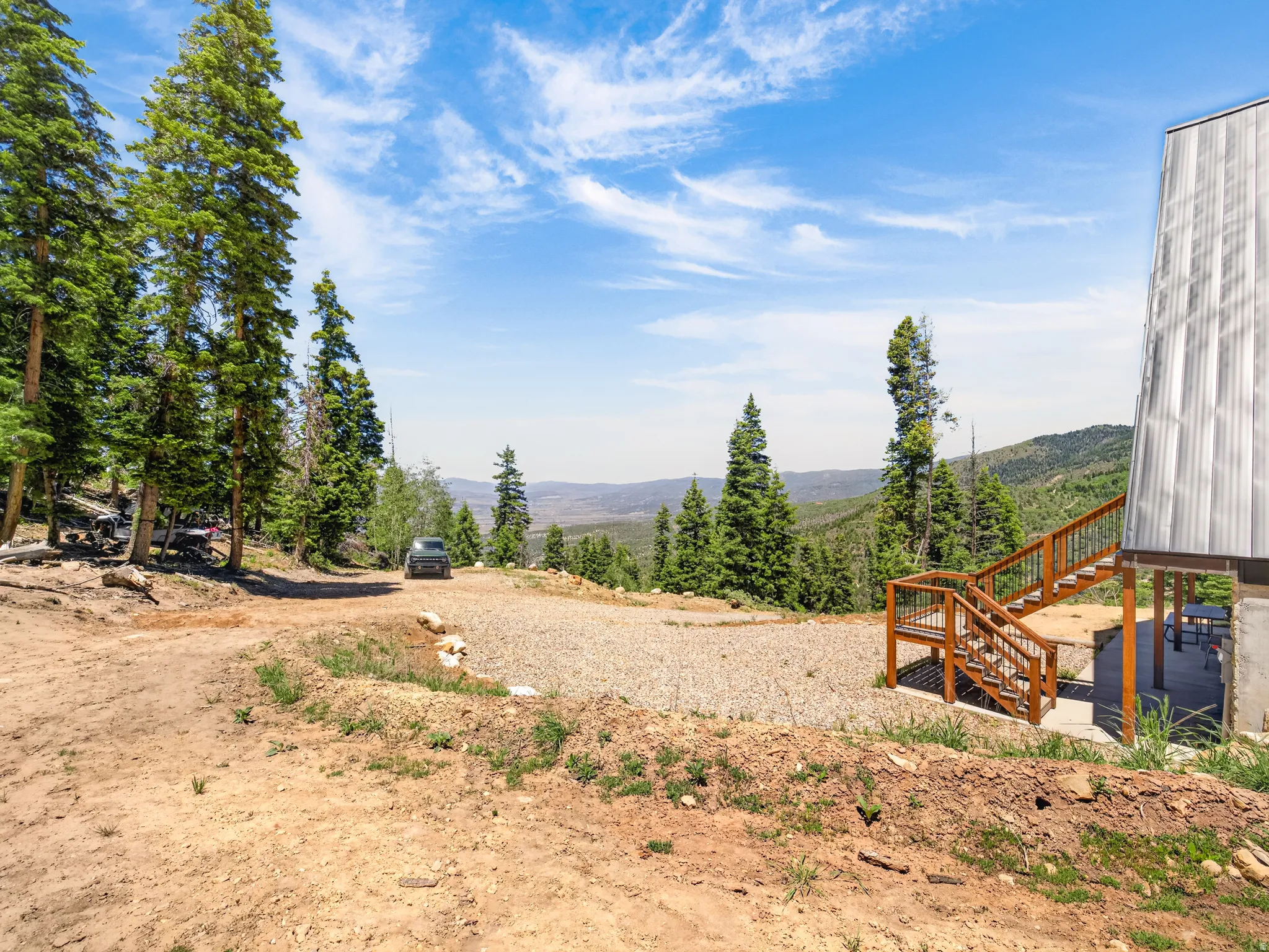 Mountainous terrain featuring dense evergreen trees and an expansive gravel parking area