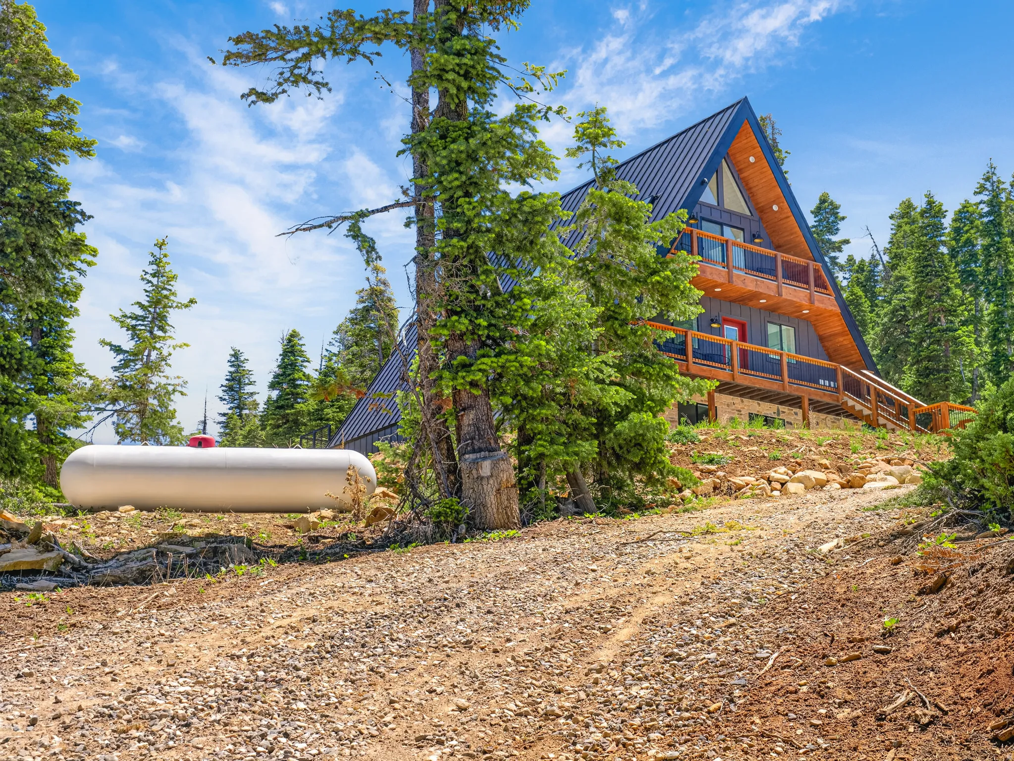 A-frame exterior with dark blue metal roofing, wood siding, multiple balconies, and a red entry door