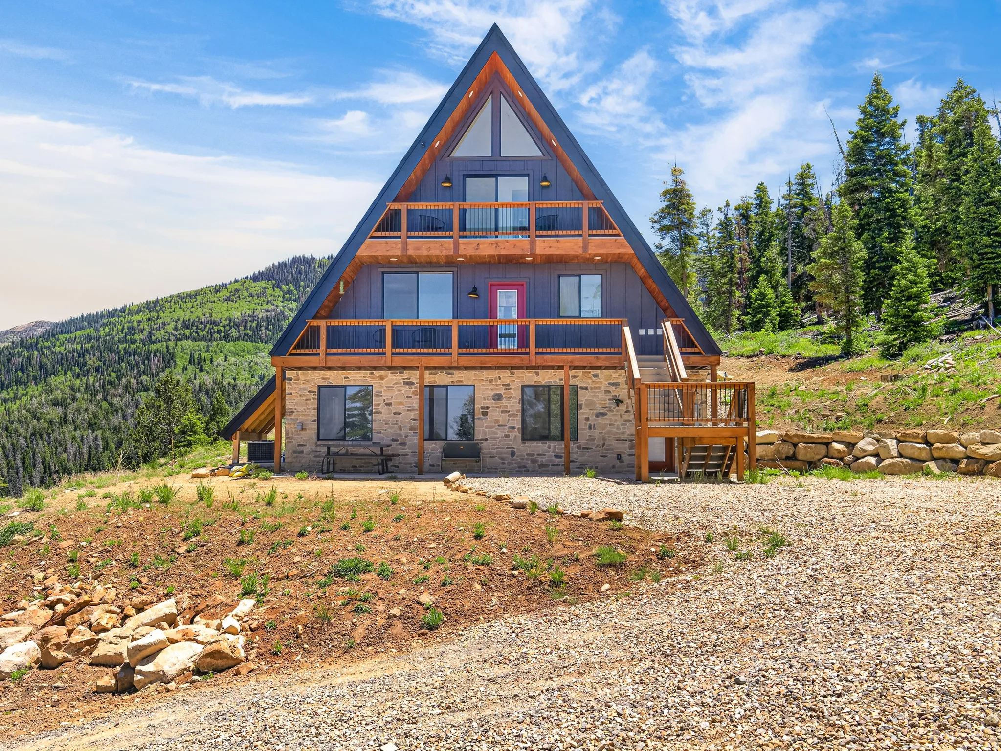 Contemporary A-frame residence featuring stone cladding, a dark siding finish, and natural wood accents