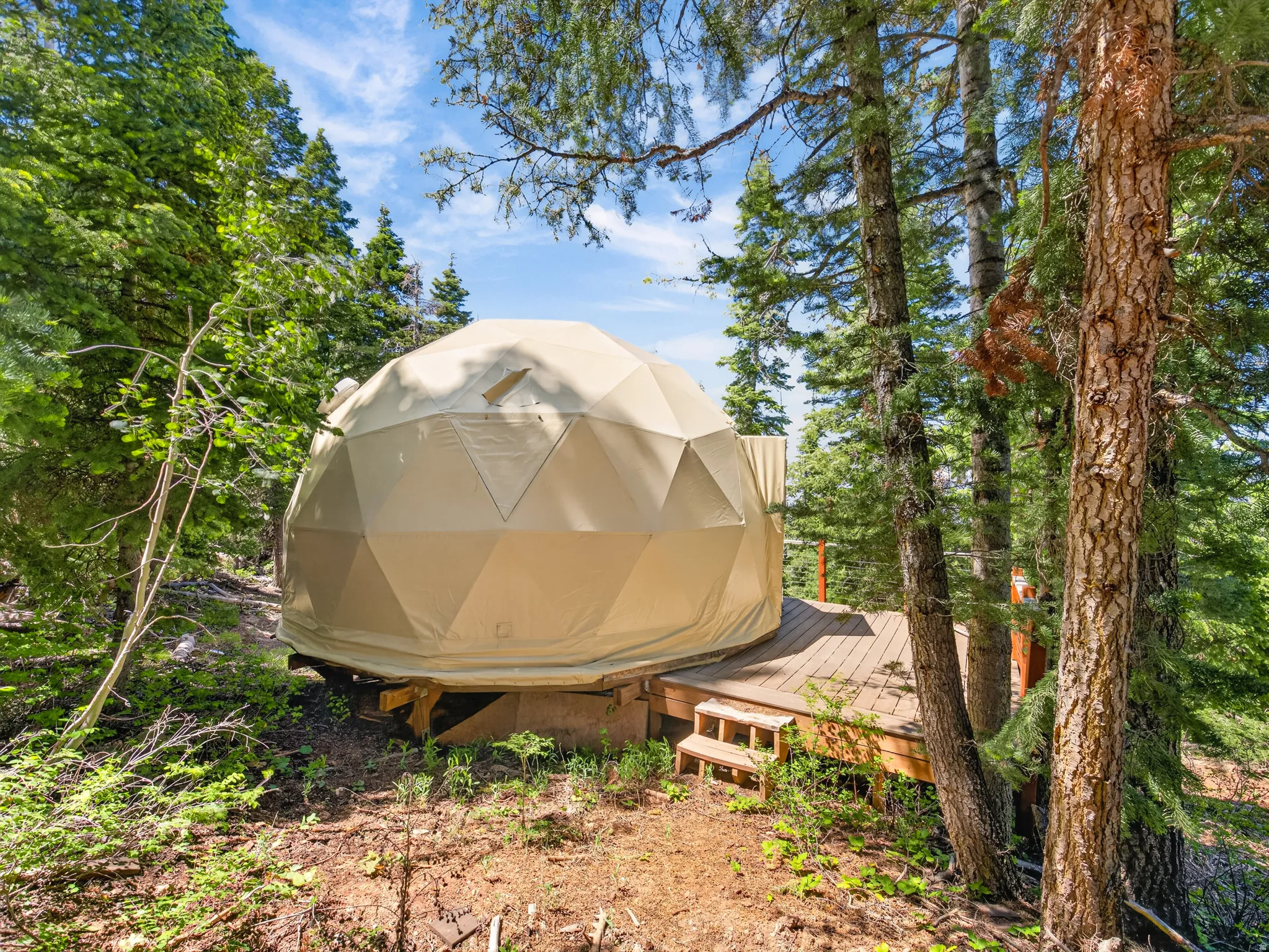 Geodesic dome structure featuring a beige canvas exterior and a private wood deck