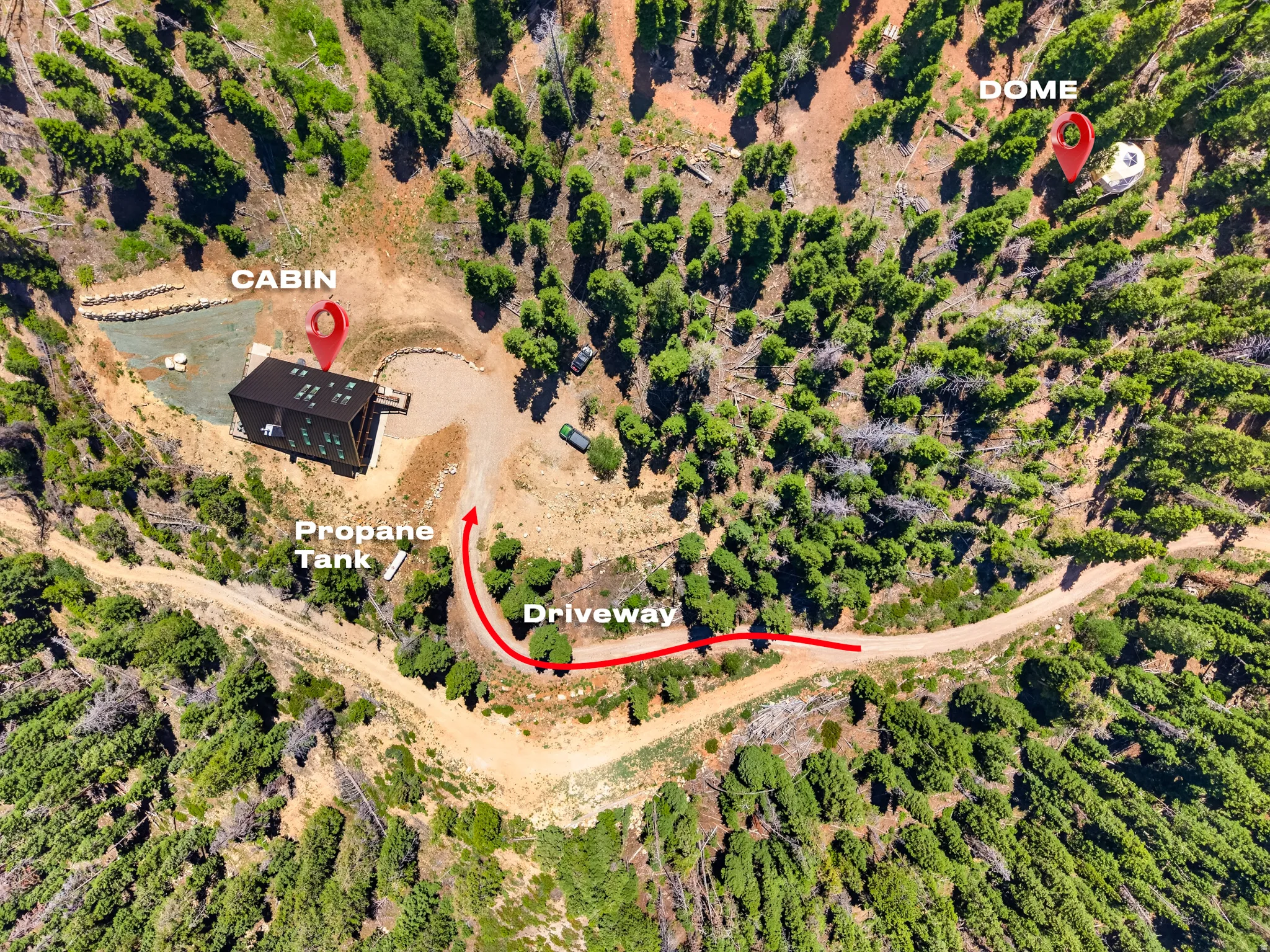 Secluded property featuring a cabin, a geodesic dome, a propane tank, and a gravel driveway, all surrounded by dense natural vegetation