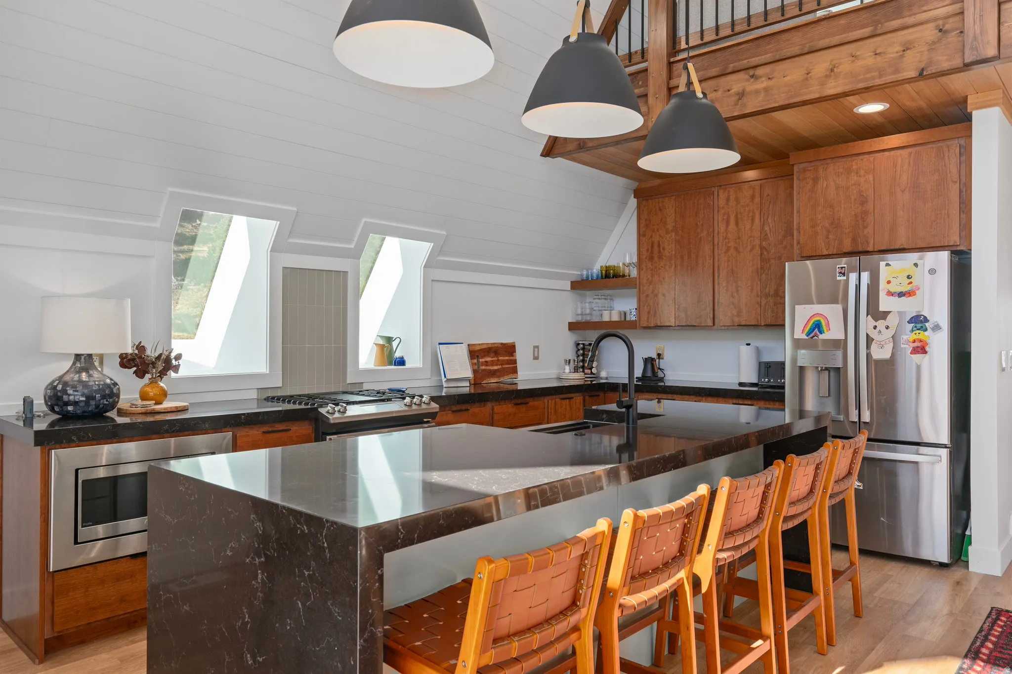 Kitchen featuring light wood-style floors, stainless steel appliances, wood finish cabinets, dark stone counters, and lofted ceiling