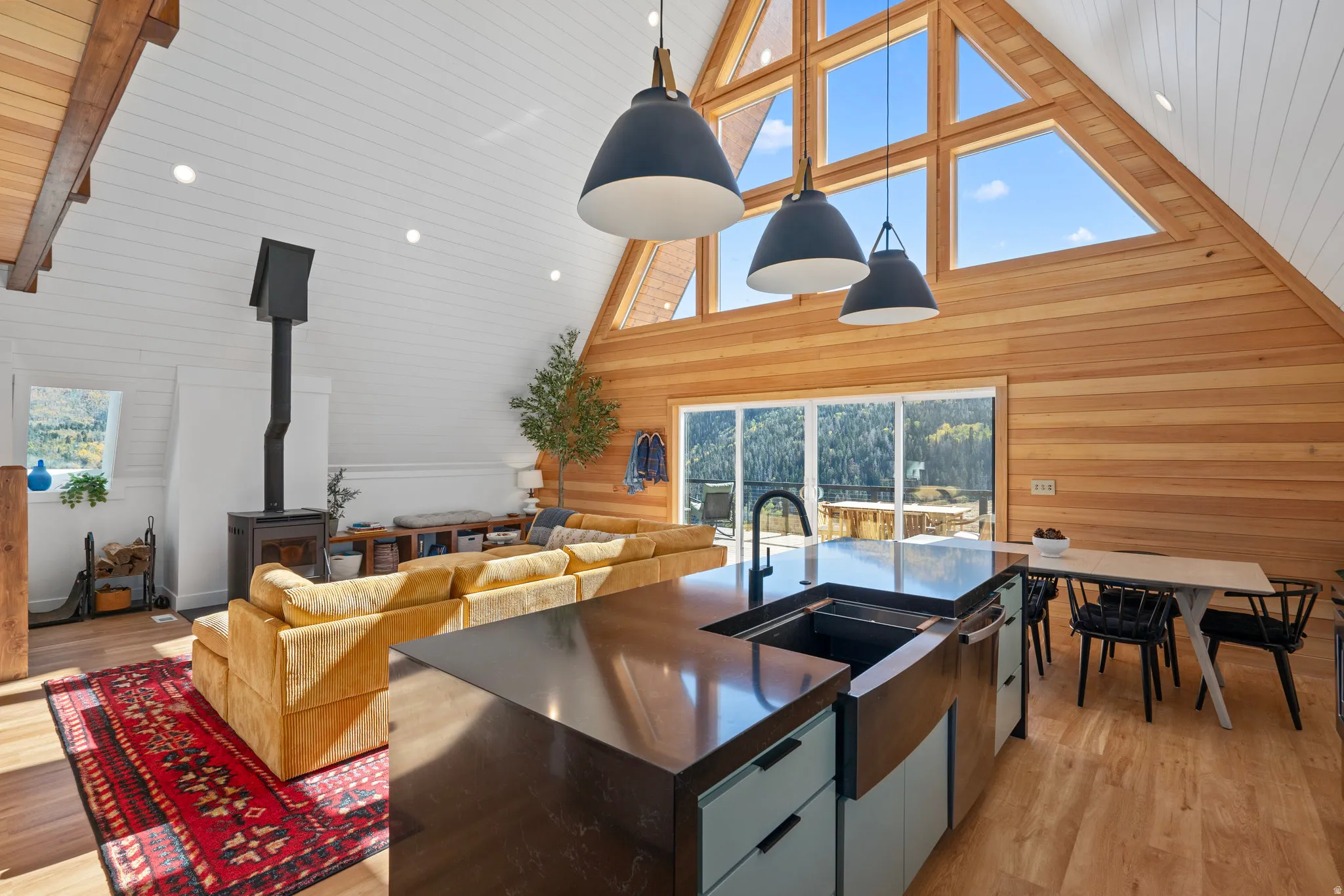Kitchen with pendant lighting, light wood-style floors, a wood stove, open floor plan, and an island with sink