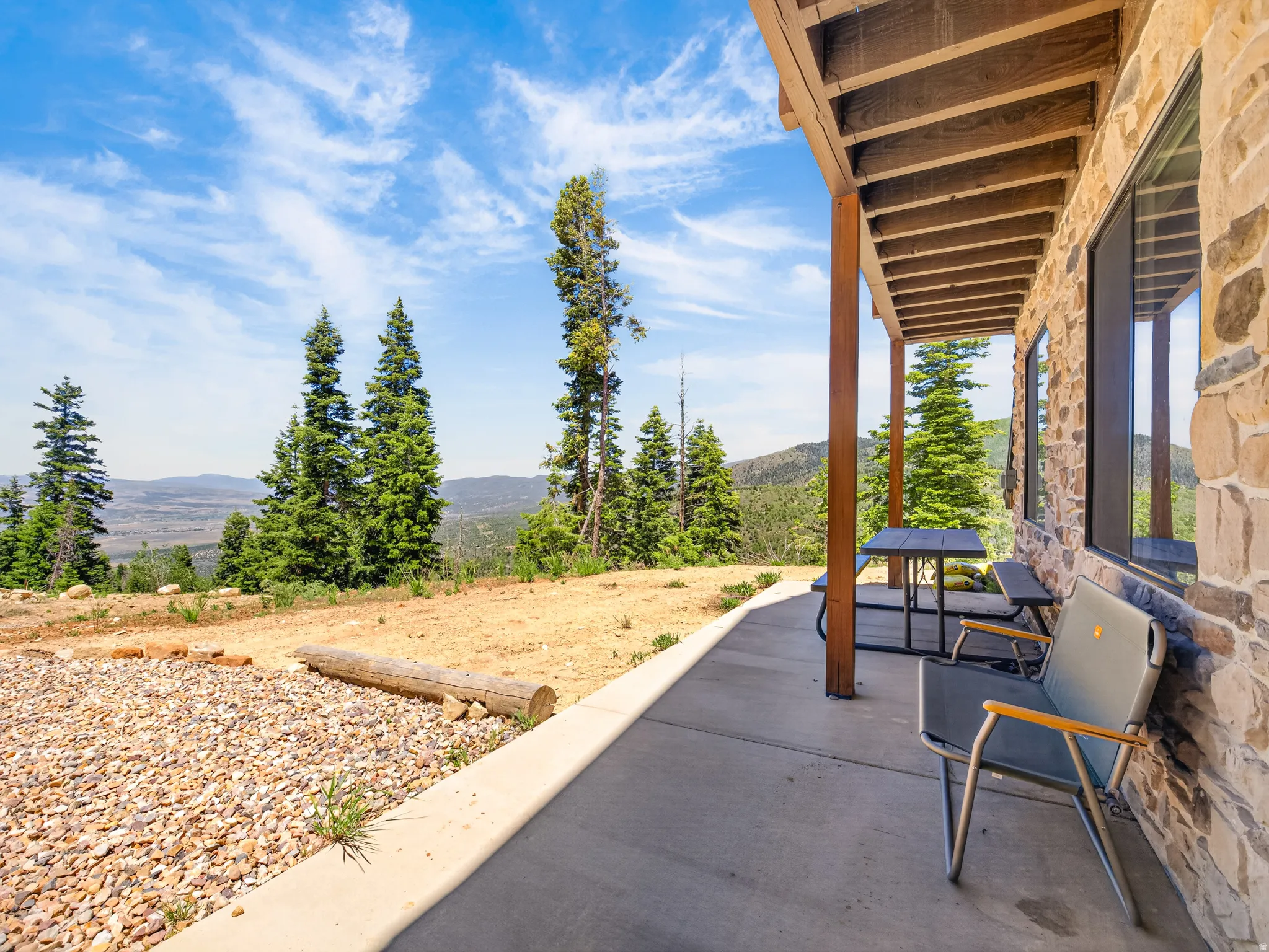 Covered patio featuring a stone-clad exterior, exposed wood beam ceiling, and a concrete slab floor
