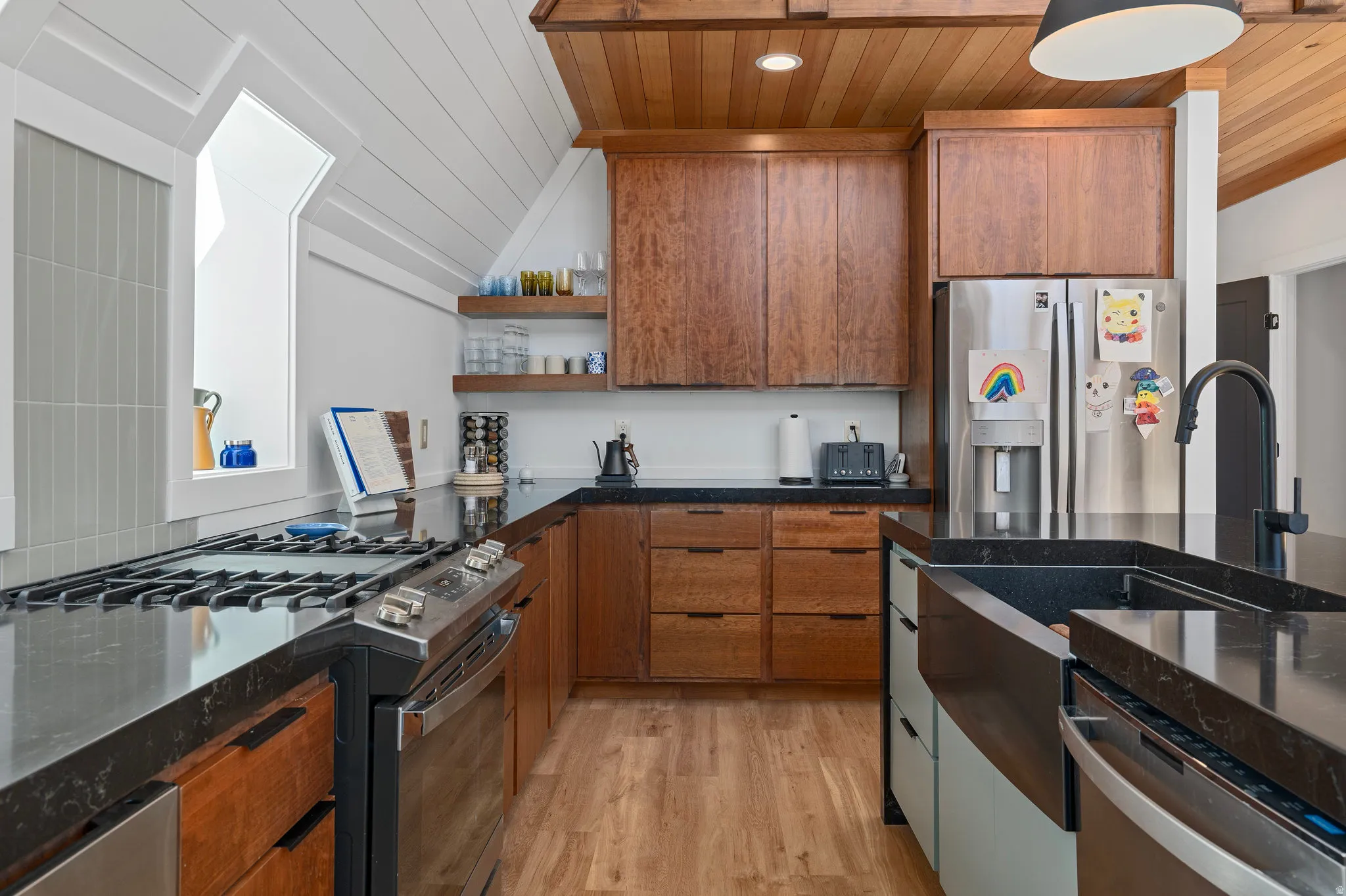 Two tone kitchen featuring stainless steel appliances, dark stone countertops, two tone cabinets, light wood-style floors, and wood ceiling