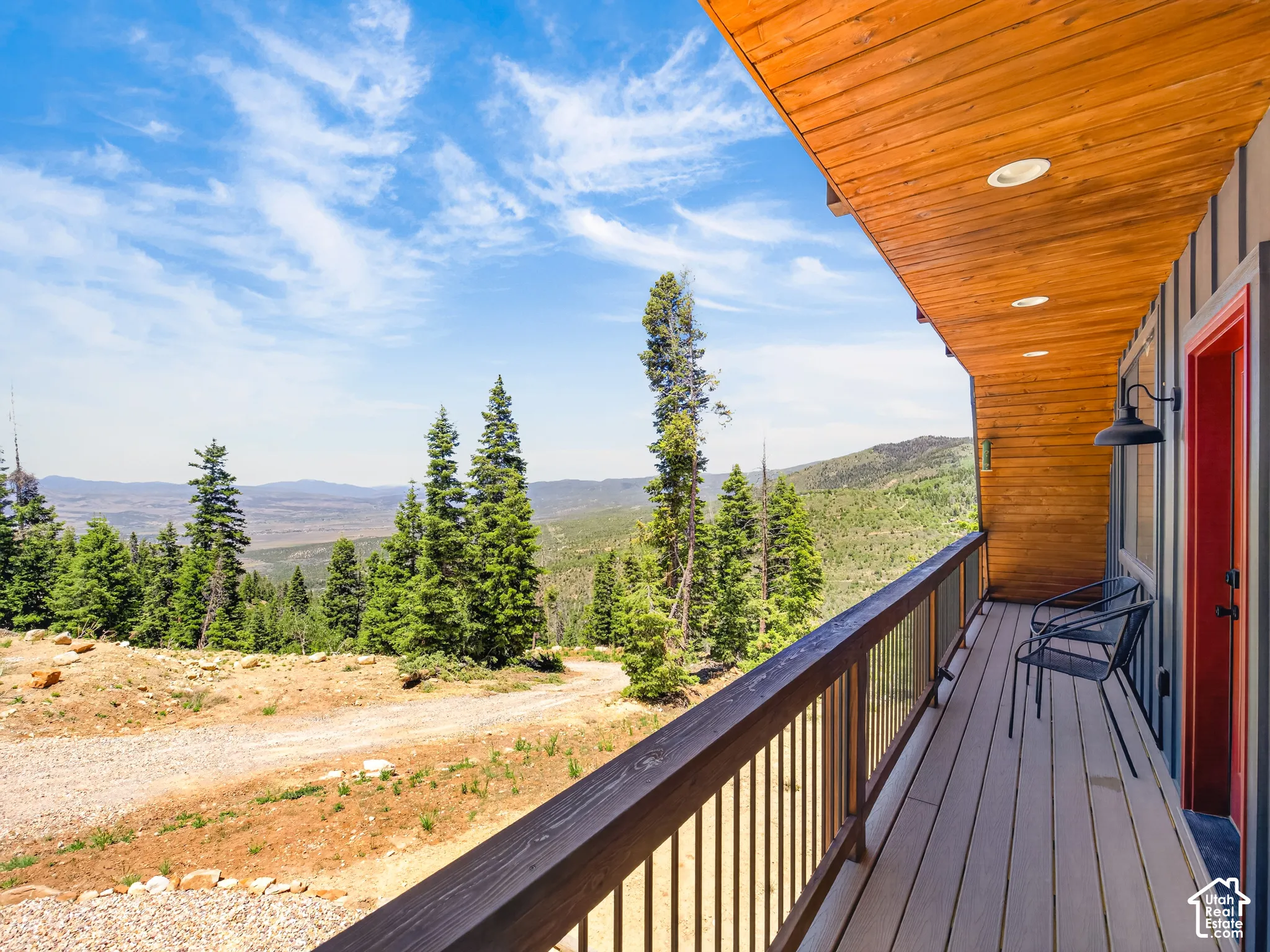 Expansive balcony featuring composite decking, wood-finish railing with glass panels, and a red entry door