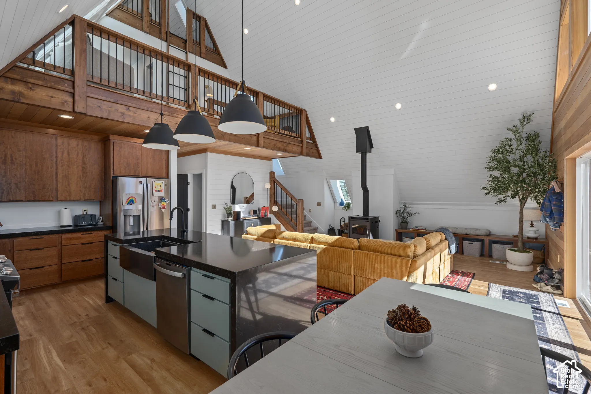 Kitchen with light wood-style flooring, modern cabinets, vaulted ceiling, open floor plan, and stainless steel appliances