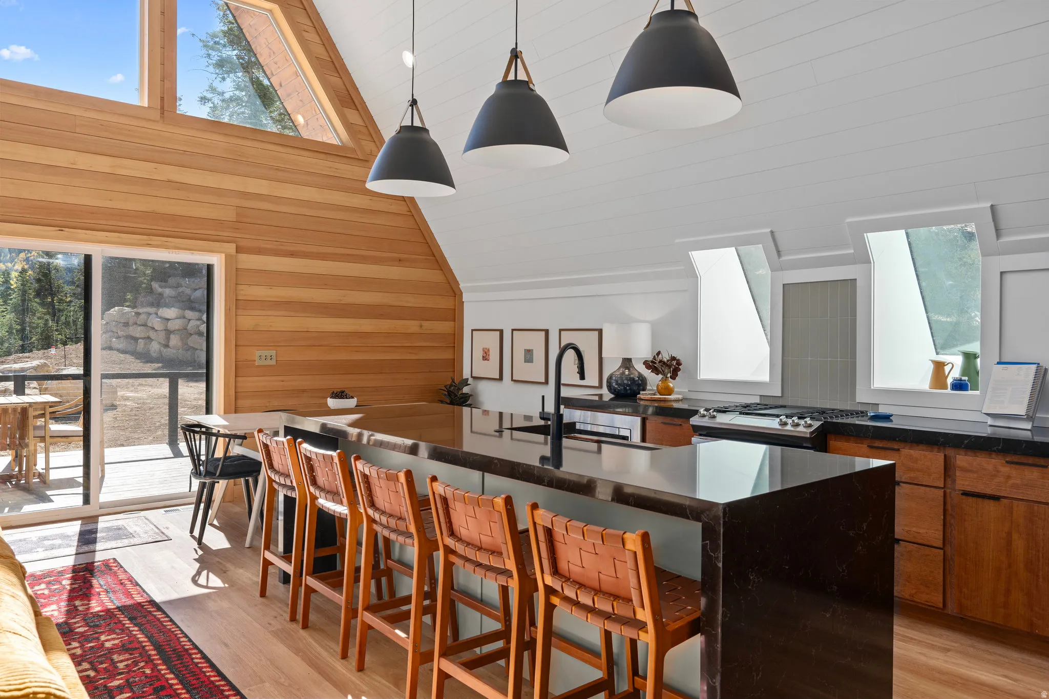 Kitchen featuring lofted ceiling, healthy amount of natural light, a breakfast bar area, wooden walls, and pendant lighting