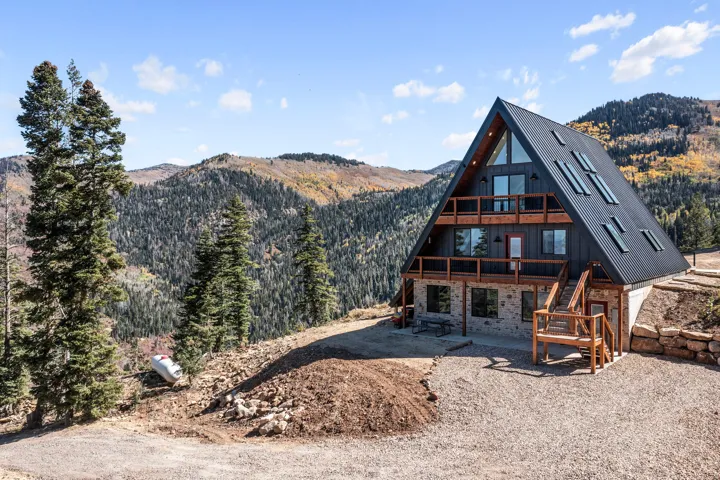 View of front of property with a mountain view, stone siding, a patio area, and a wooded view
