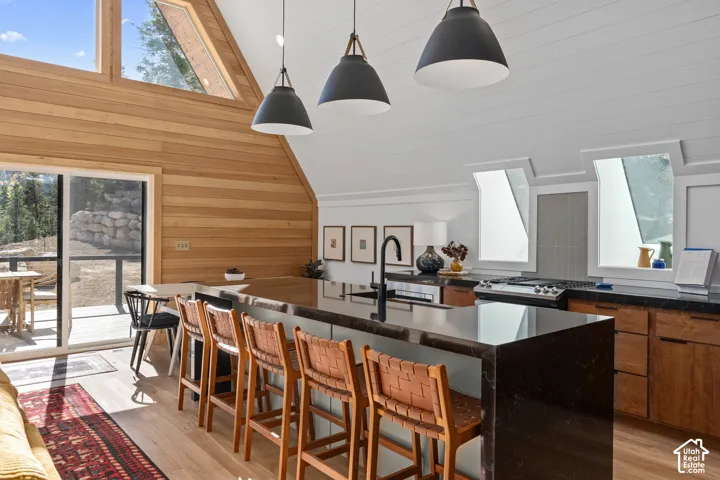Kitchen featuring lofted ceiling, healthy amount of natural light, a breakfast bar area, wooden walls, and pendant lighting