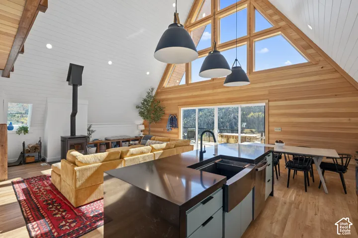Kitchen with pendant lighting, light wood-style floors, a wood stove, open floor plan, and an island with sink