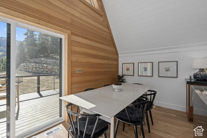 Dining space featuring wooden walls, light wood-type flooring, and vaulted ceiling