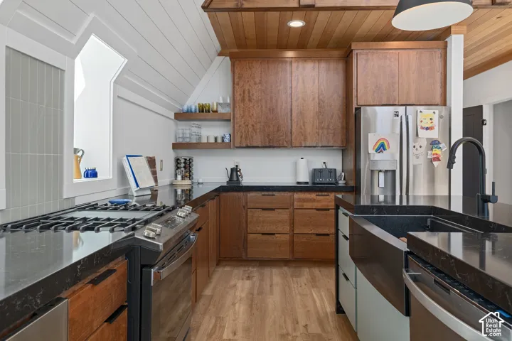 Two tone kitchen featuring stainless steel appliances, dark stone countertops, two tone cabinets, light wood-style floors, and wood ceiling
