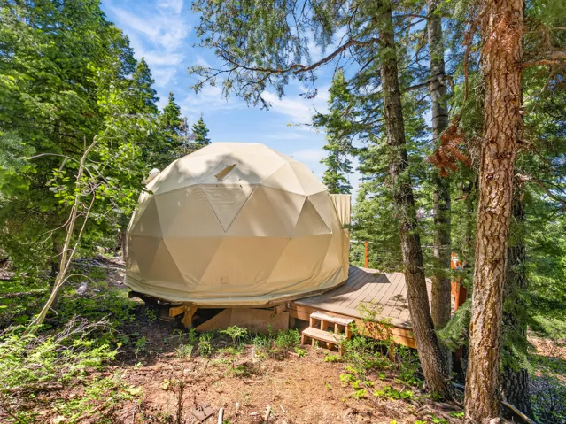 Geodesic dome structure featuring a beige canvas exterior and a private wood deck