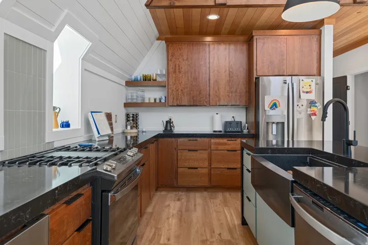 Two tone kitchen featuring stainless steel appliances, dark stone countertops, two tone cabinets, light wood-style floors, and wood ceiling