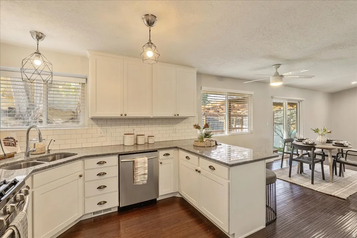 Kitchen with dark stone countertops, a peninsula, stainless steel appliances, dark wood-type flooring, and a ceiling fan