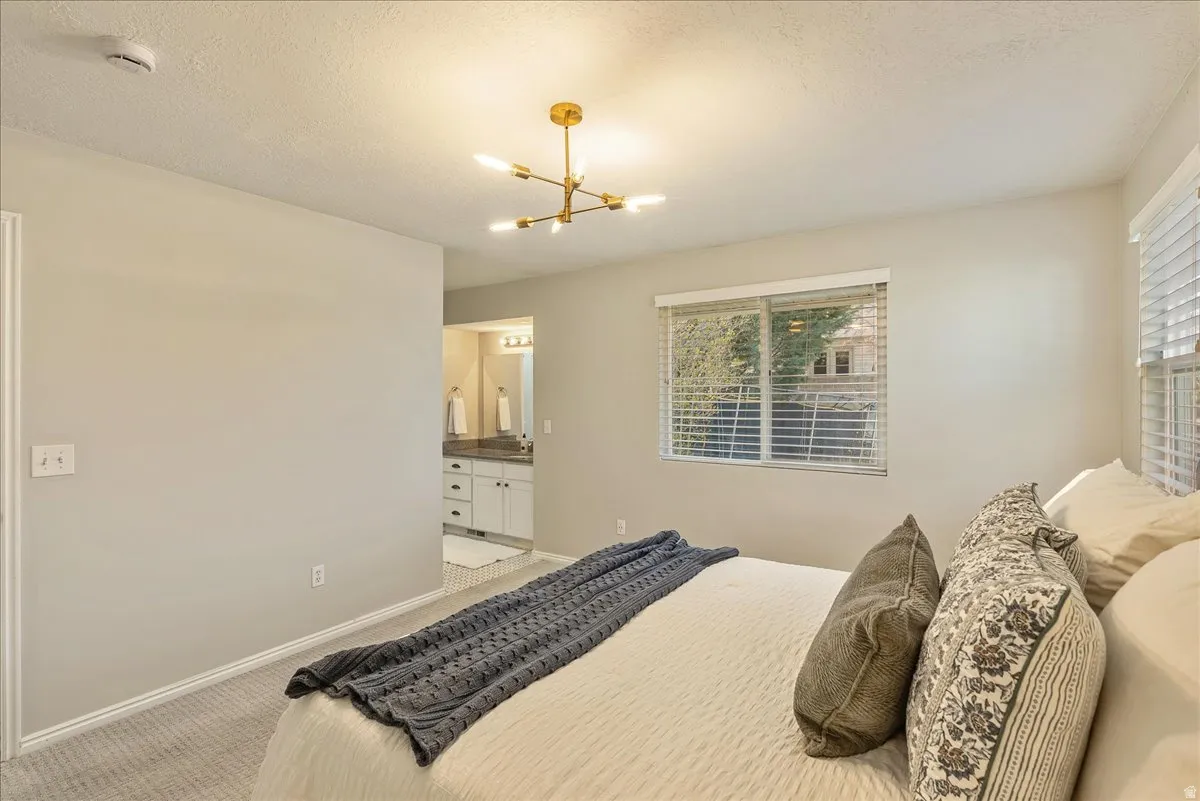 Bedroom with light carpet, a textured ceiling, ensuite bathroom, and hanging lights