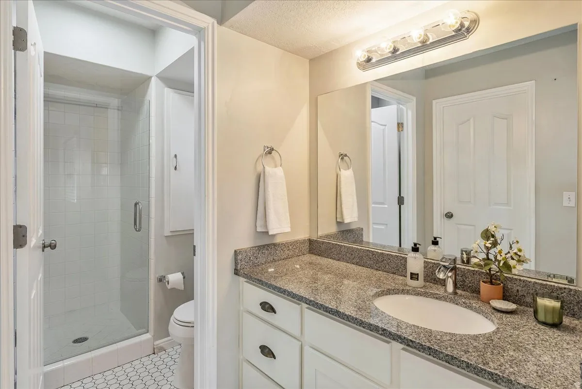 Full bathroom with vanity, a shower stall, a textured ceiling, and light tile patterned flooring