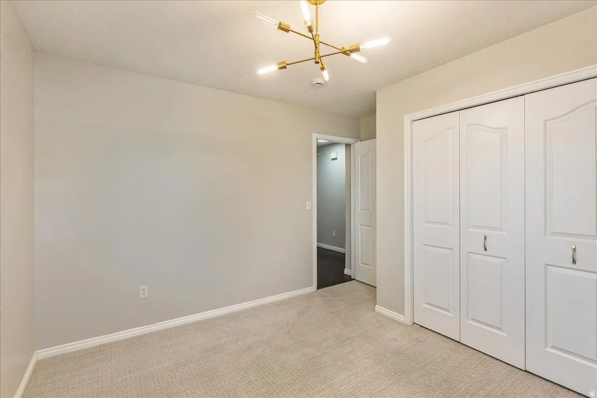 Unfurnished bedroom featuring light colored carpet, a closet, and hanging lights