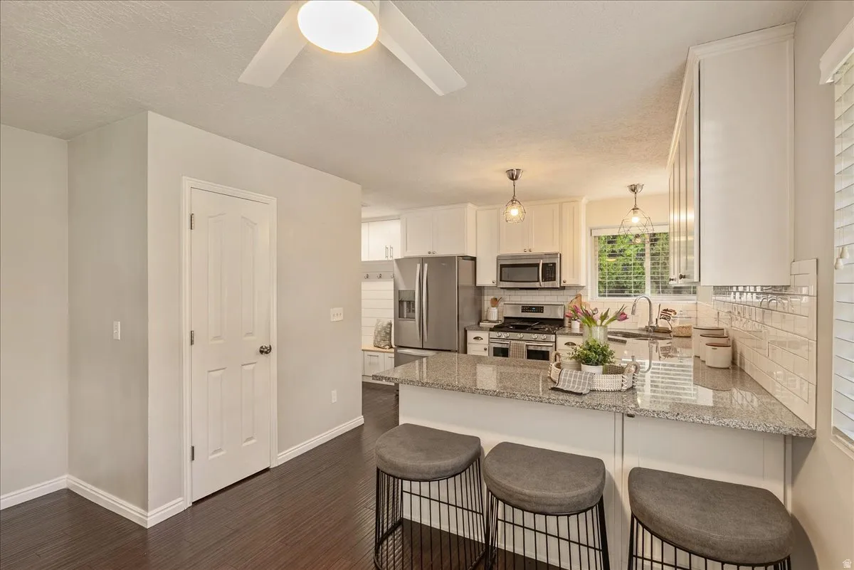 Kitchen with white cabinets, stainless steel appliances, light stone counters, a breakfast bar area, and a textured ceiling
