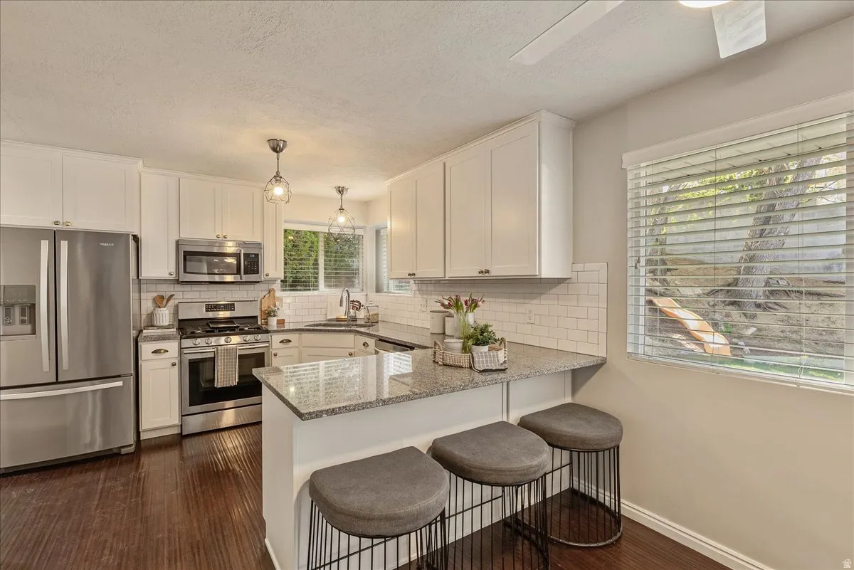 Kitchen with stainless steel appliances, light stone countertops, dark wood-type flooring, white cabinets, and a kitchen bar