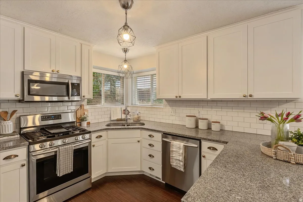 Kitchen featuring stainless steel appliances, white cabinetry, dark wood finished floors, dark stone counters, and a textured ceiling