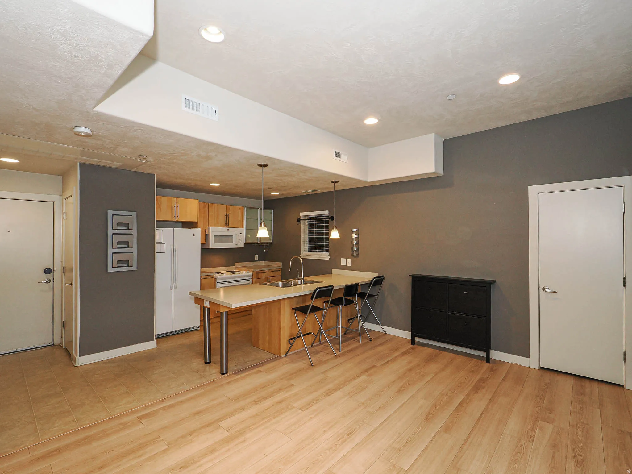 Kitchen featuring a kitchen breakfast bar, a peninsula, white appliances, decorative light fixtures, and light countertops