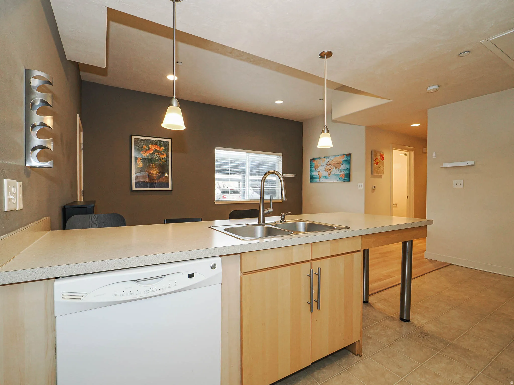 Kitchen featuring white dishwasher, light countertops, a peninsula, light wood finish cabinetry, and a kitchen breakfast bar