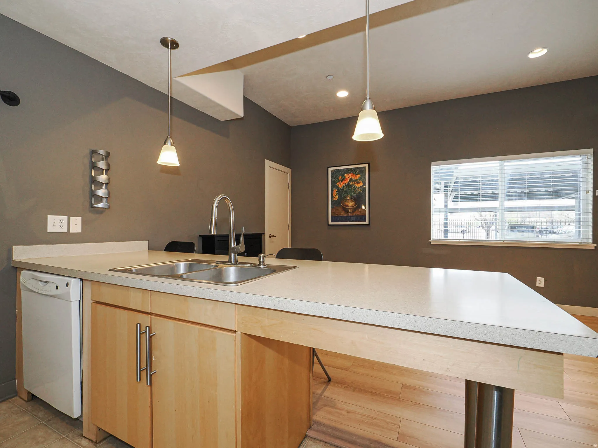 Kitchen with dishwasher, light countertops, light wood finish cabinets, a peninsula, and decorative light fixtures