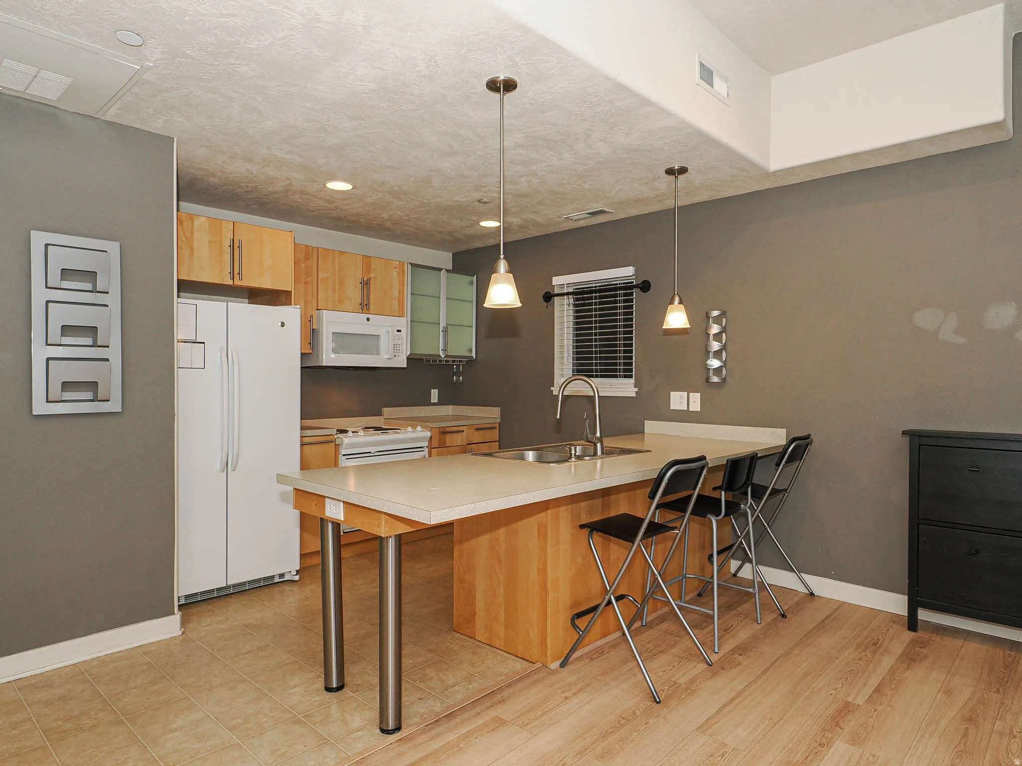 Kitchen with a peninsula, a breakfast bar, white appliances, light countertops, and hanging light fixtures