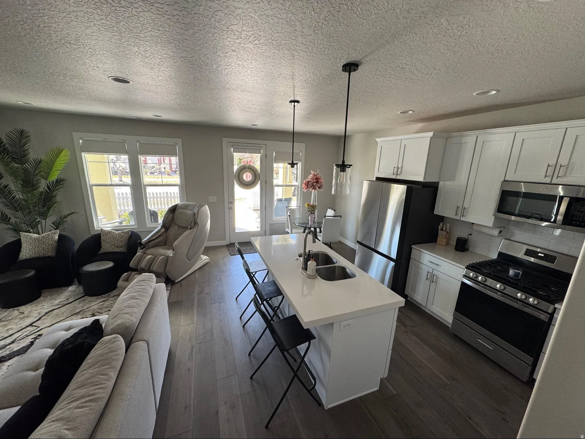Kitchen featuring open floor plan, a kitchen breakfast bar, stainless steel appliances, dark wood-style floors, and white cabinetry