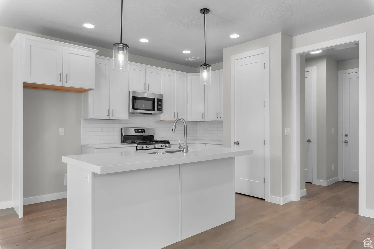 Kitchen featuring stainless steel appliances, an island with sink, white cabinetry, and tasteful backsplash