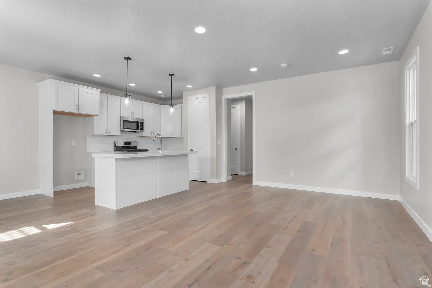 Kitchen featuring white cabinets, pendant lighting, stainless steel appliances, light wood-style floors, and a center island with sink